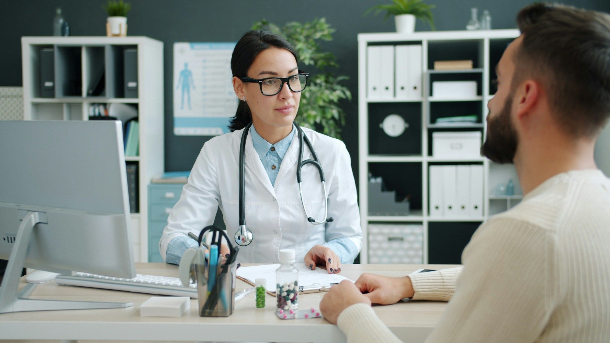 A doctor in a white coat talking with a patient across her desk
